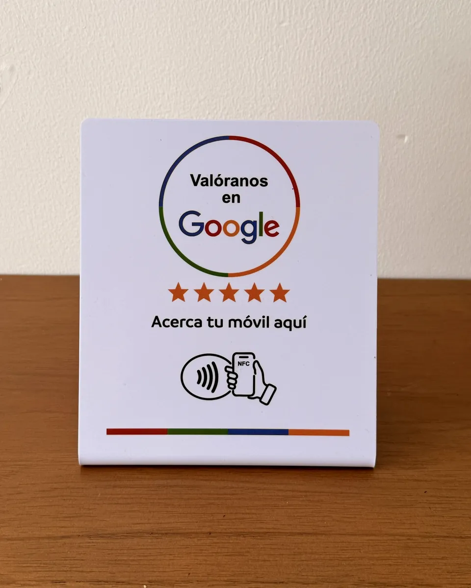 Soporte NFC blanco sobre una mesa, con el texto Valóranos en Google y Acerca tu móvil aquí